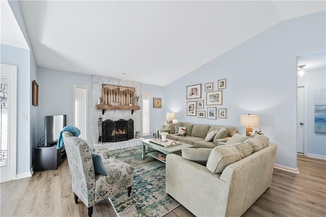 living room featuring baseboards, vaulted ceiling, light wood-type flooring, and a fireplace