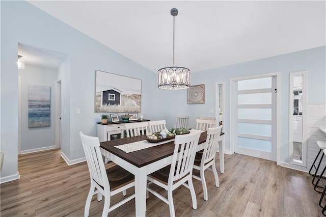 dining area featuring baseboards, vaulted ceiling, light wood-style floors, and an inviting chandelier