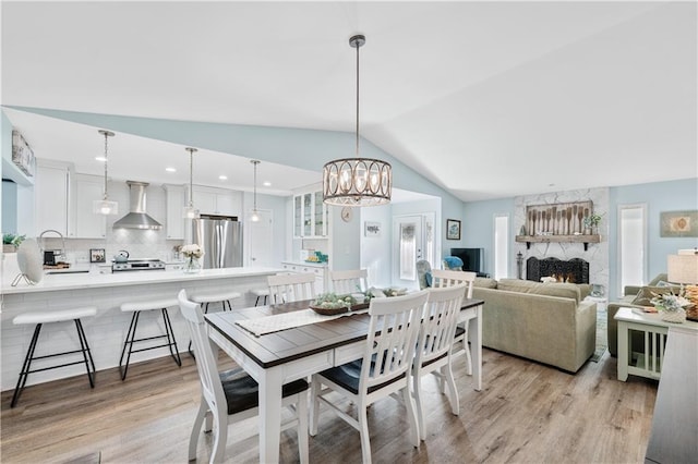 dining room featuring lofted ceiling, a notable chandelier, light wood-style floors, and a fireplace