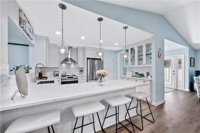 kitchen featuring decorative backsplash, a sink, wall chimney range hood, a peninsula, and appliances with stainless steel finishes