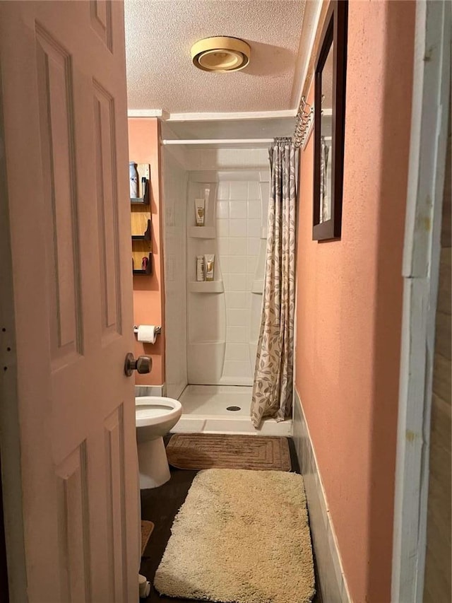 full bath with toilet, a shower stall, and a textured ceiling