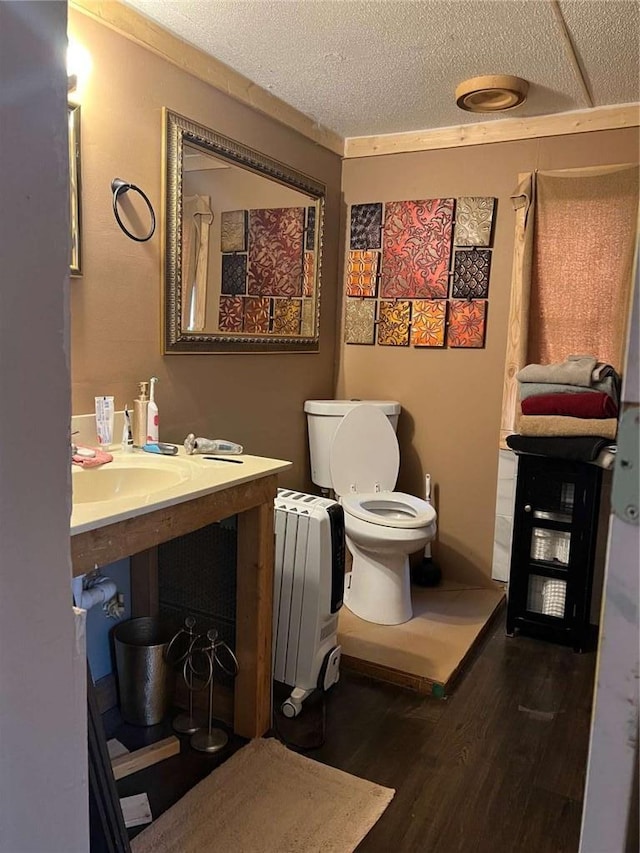 bathroom with vanity, wood finished floors, radiator heating unit, a textured ceiling, and toilet