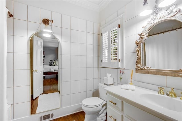 ensuite bathroom with crown molding, tile walls, visible vents, toilet, and vanity