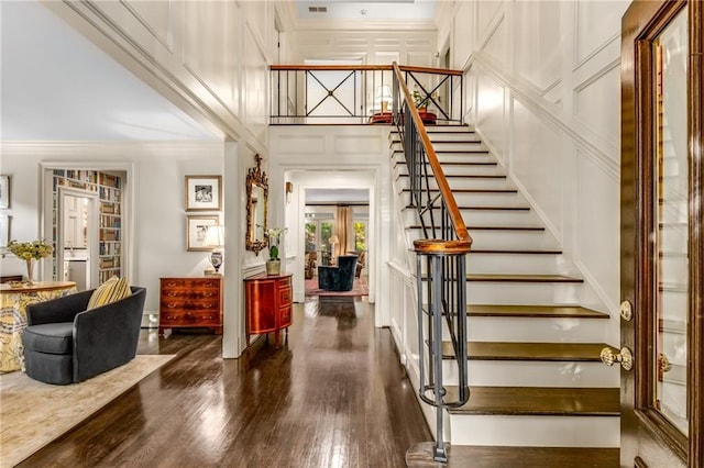 entryway featuring ornamental molding, wood finished floors, stairs, a high ceiling, and a decorative wall