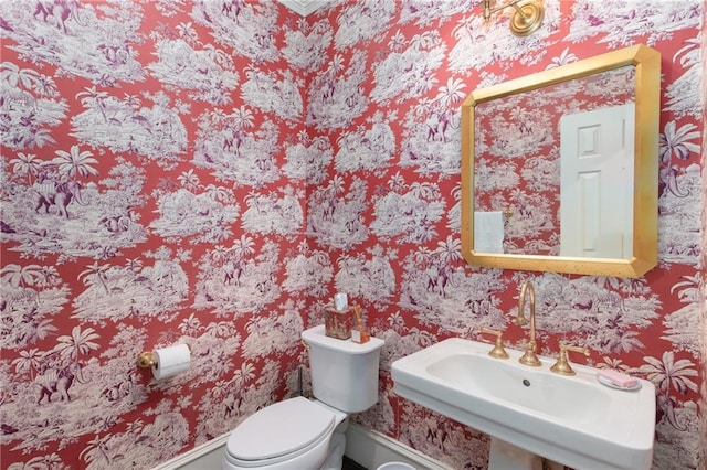 bathroom with a sink, toilet, and wallpapered walls