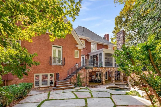 rear view of house featuring brick siding, a chimney, stairway, a sunroom, and a patio area