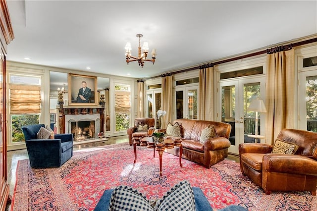 living area featuring a healthy amount of sunlight, a fireplace with raised hearth, a notable chandelier, and french doors