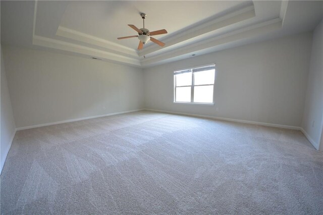 empty room with ceiling fan, baseboards, ornamental molding, light carpet, and a raised ceiling