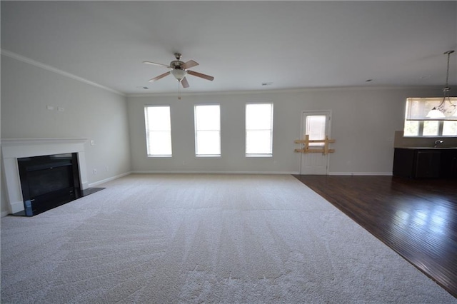 unfurnished living room with a fireplace with flush hearth, crown molding, baseboards, and wood finished floors