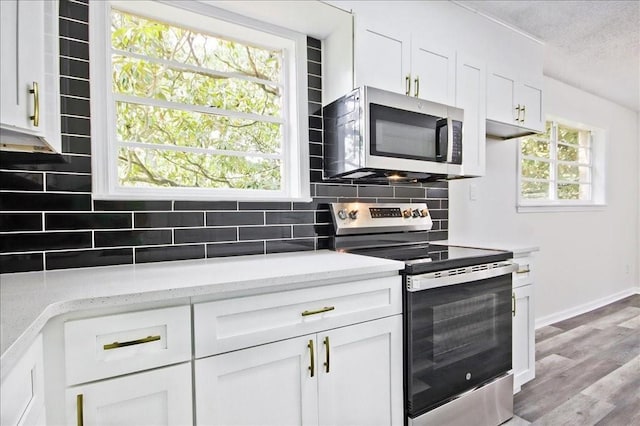 kitchen with appliances with stainless steel finishes, white cabinets, light wood finished floors, and tasteful backsplash
