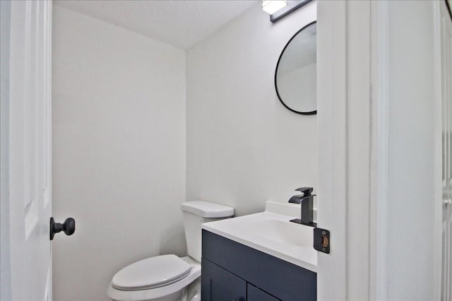 half bathroom featuring vanity, a textured ceiling, and toilet