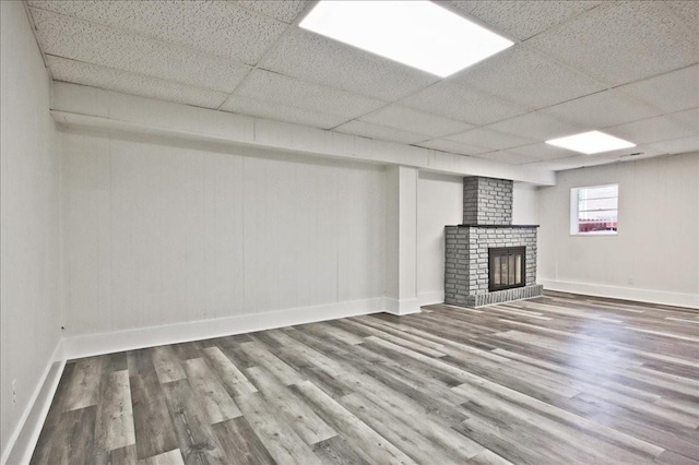 below grade area featuring wood finished floors, baseboards, a brick fireplace, and a drop ceiling
