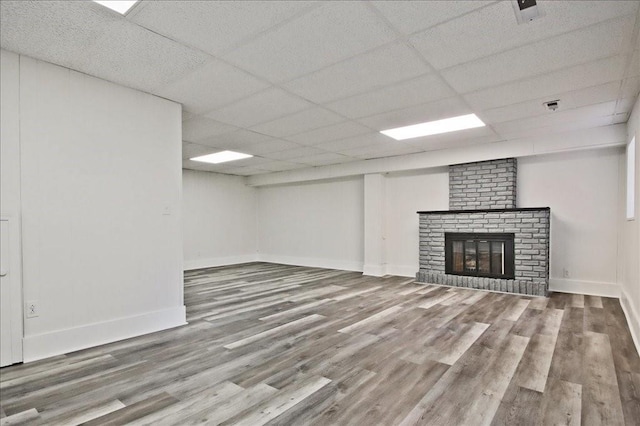 unfurnished living room with baseboards, a paneled ceiling, wood finished floors, and a fireplace