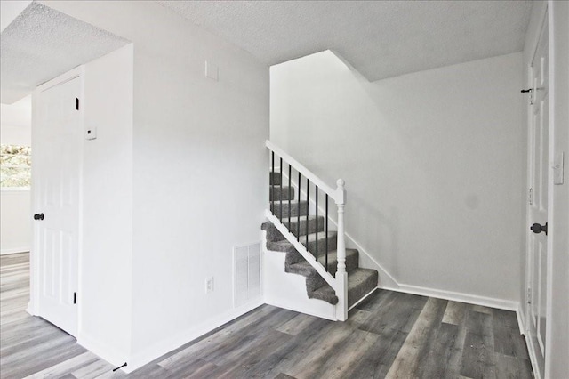 stairs featuring visible vents, baseboards, a textured ceiling, and wood finished floors