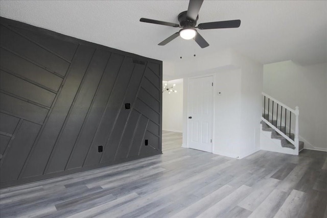 unfurnished living room with baseboards, ceiling fan with notable chandelier, stairs, and wood finished floors