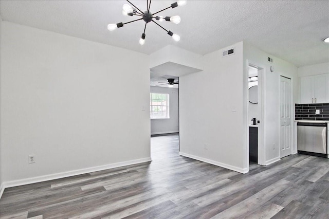 unfurnished living room featuring a textured ceiling, ceiling fan with notable chandelier, baseboards, wood finished floors, and visible vents