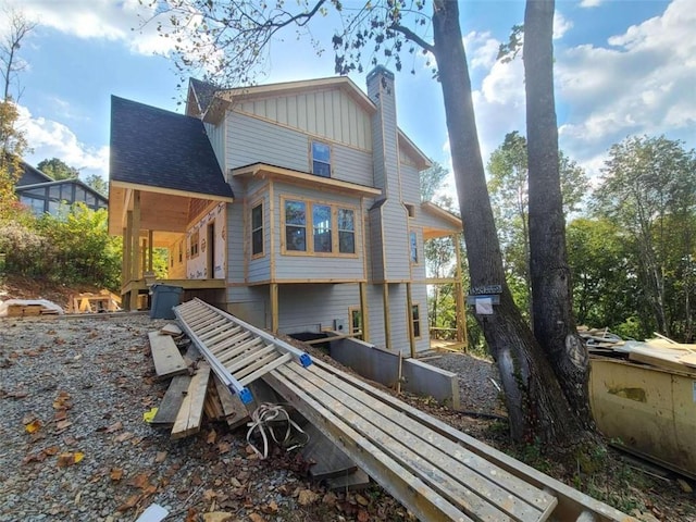 back of house featuring board and batten siding, roof with shingles, and a chimney