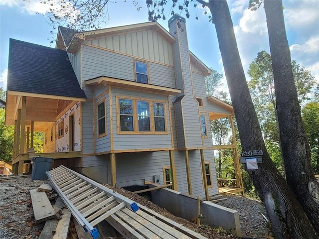 rear view of house with roof with shingles, board and batten siding, and a chimney