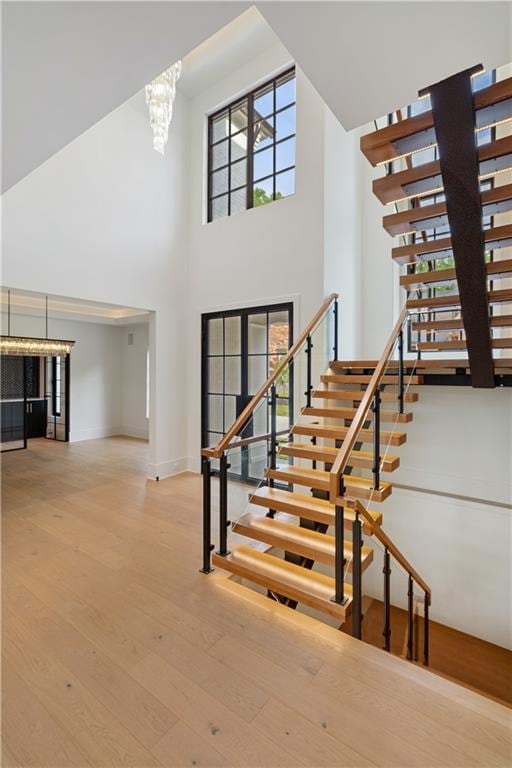 staircase featuring a notable chandelier, a towering ceiling, french doors, and hardwood / wood-style flooring