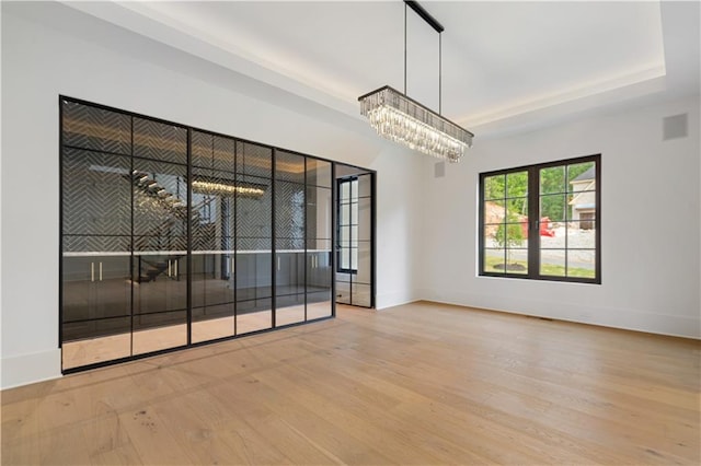 unfurnished room featuring an inviting chandelier, light hardwood / wood-style flooring, and a tray ceiling