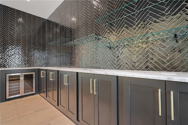 bar featuring gray cabinets, light hardwood / wood-style floors, light stone counters, and backsplash