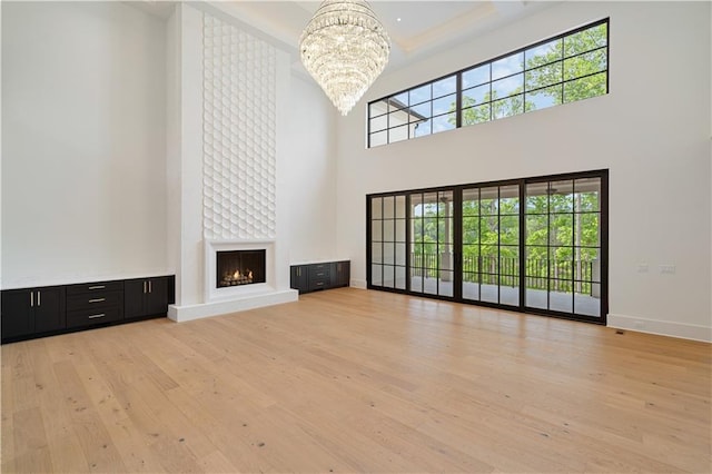 unfurnished living room featuring a towering ceiling, a healthy amount of sunlight, a chandelier, and light hardwood / wood-style flooring