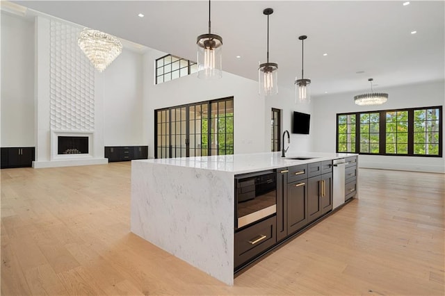 kitchen with light hardwood / wood-style floors, a center island with sink, hanging light fixtures, sink, and a chandelier