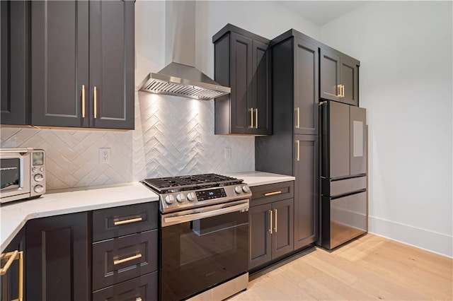 kitchen with stainless steel appliances, wall chimney range hood, light hardwood / wood-style floors, and tasteful backsplash