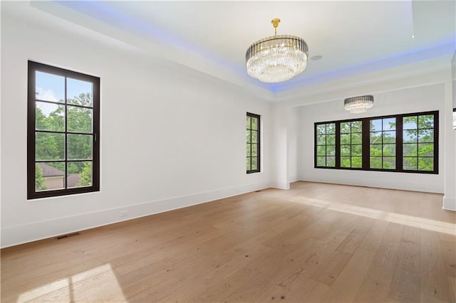 spare room featuring a healthy amount of sunlight, a notable chandelier, and light hardwood / wood-style flooring