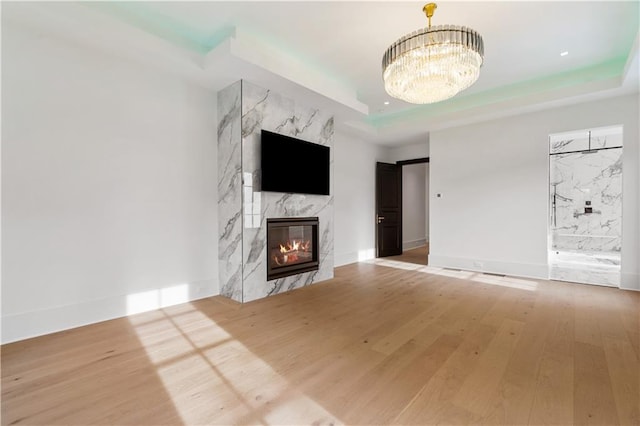 unfurnished living room with a premium fireplace, an inviting chandelier, hardwood / wood-style floors, and a tray ceiling