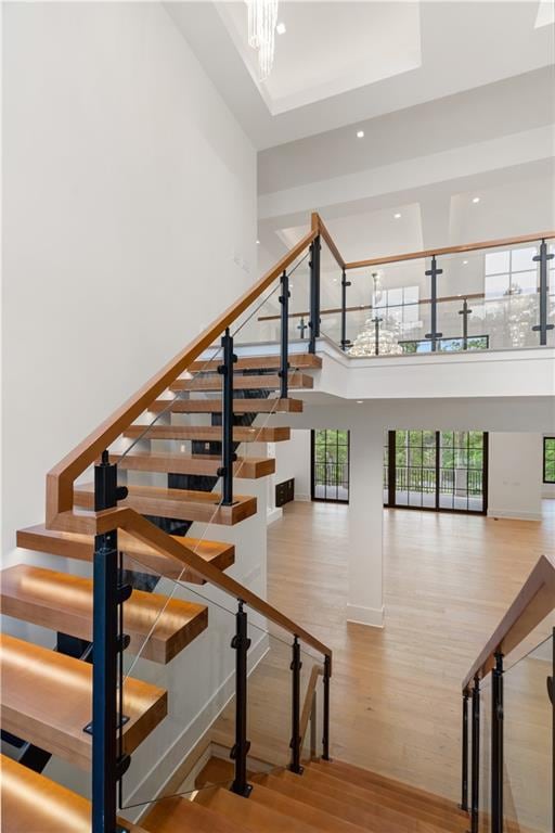 staircase featuring a towering ceiling, an inviting chandelier, and hardwood / wood-style flooring