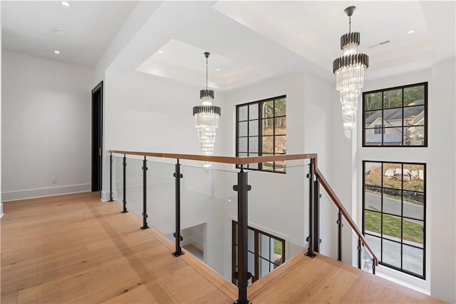 corridor featuring a tray ceiling, light wood-type flooring, and a notable chandelier