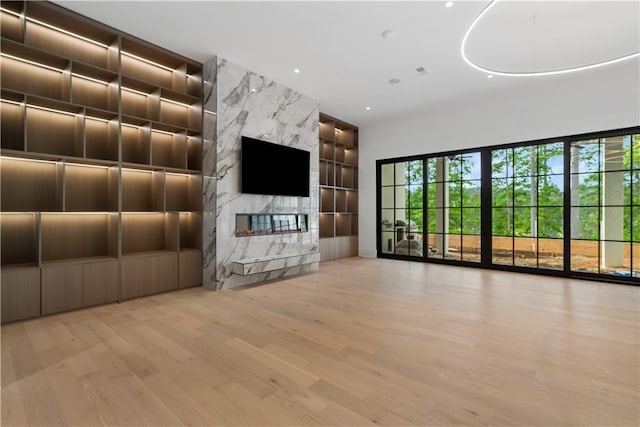 unfurnished living room featuring a premium fireplace, light hardwood / wood-style floors, and built in shelves