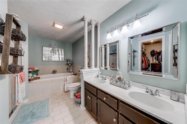 bathroom featuring vanity, a textured ceiling, tile patterned floors, tiled bath, and ornate columns