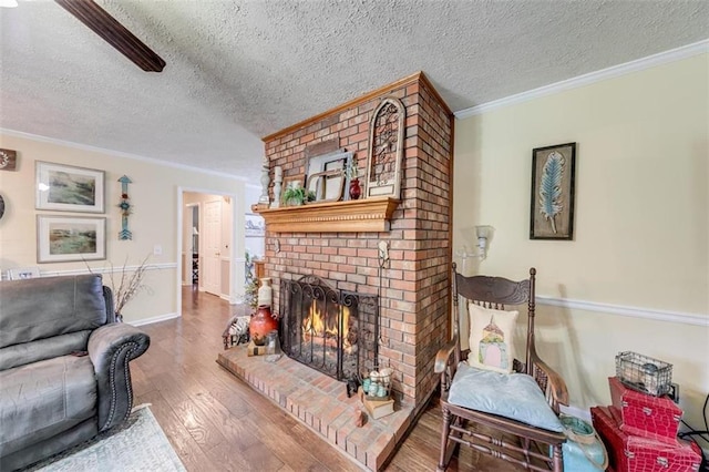 living room with wood-type flooring, a textured ceiling, a brick fireplace, and ornamental molding