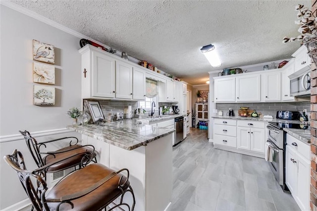 kitchen with light stone counters, stainless steel appliances, kitchen peninsula, and white cabinetry