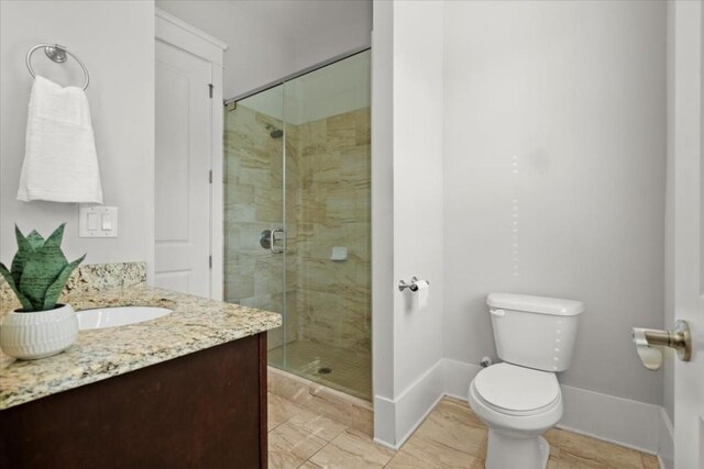 bathroom with a stall shower, vanity, toilet, and baseboards