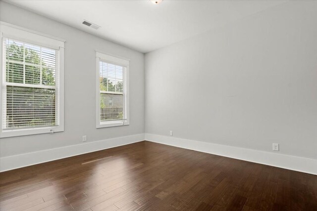 spare room with baseboards, visible vents, and dark wood finished floors