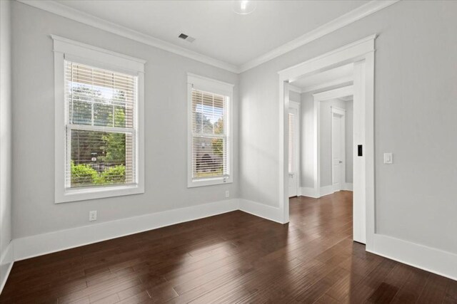 unfurnished room with ornamental molding, visible vents, baseboards, and dark wood-style floors