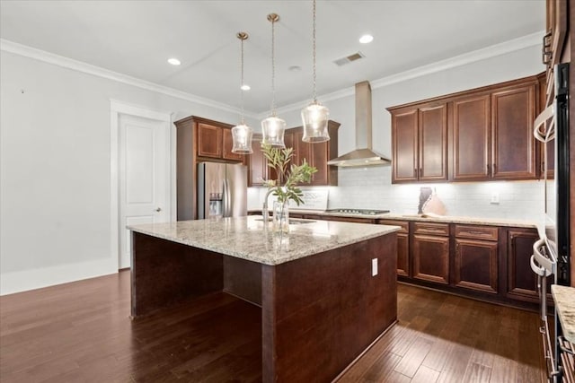 kitchen featuring light stone counters, stainless steel appliances, a kitchen island with sink, a sink, and wall chimney exhaust hood