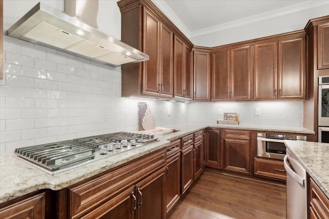 kitchen featuring light stone counters, stainless steel appliances, ornamental molding, wall chimney range hood, and dark wood finished floors