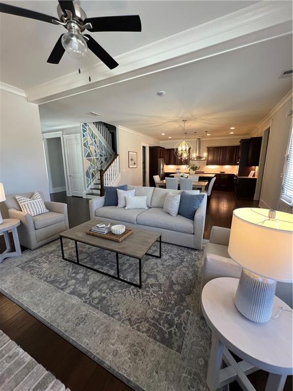 living room featuring ceiling fan with notable chandelier, visible vents, stairway, dark wood finished floors, and crown molding