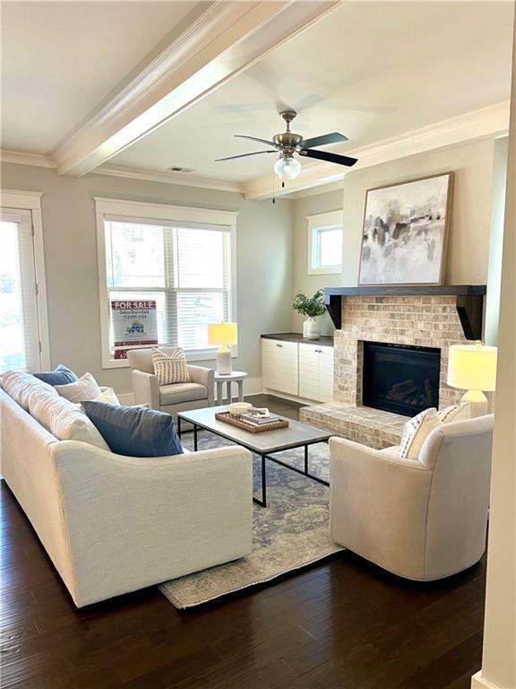 living room with a fireplace, visible vents, ornamental molding, beam ceiling, and dark wood finished floors