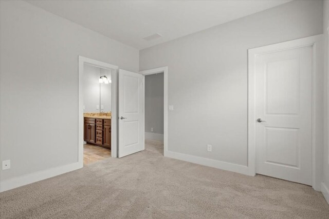 unfurnished bedroom featuring light carpet, baseboards, and connected bathroom