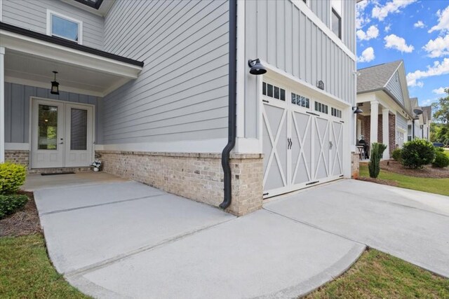 doorway to property featuring concrete driveway, french doors, board and batten siding, and brick siding