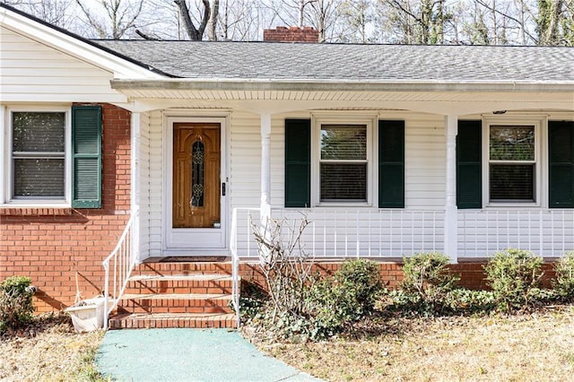 view of exterior entry featuring a shingled roof, a chimney, and brick siding