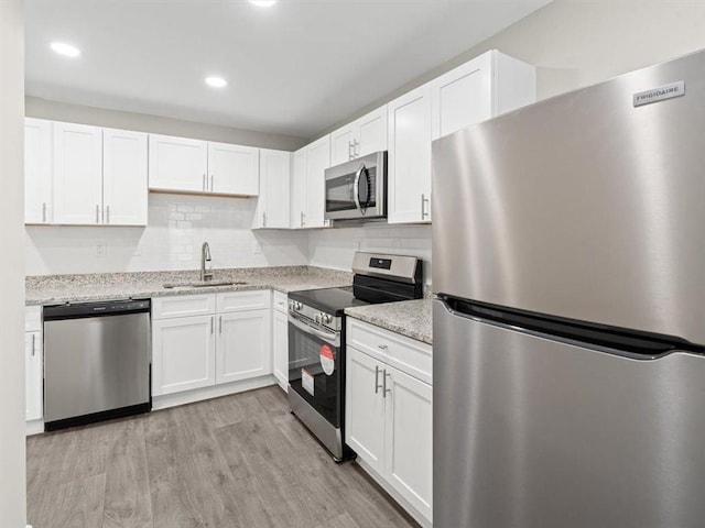 kitchen with appliances with stainless steel finishes, white cabinetry, light stone countertops, light hardwood / wood-style flooring, and sink