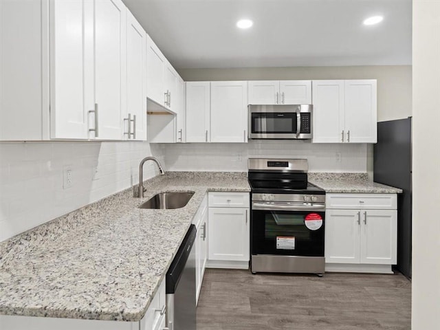 kitchen featuring appliances with stainless steel finishes, light stone counters, white cabinets, light wood-type flooring, and sink