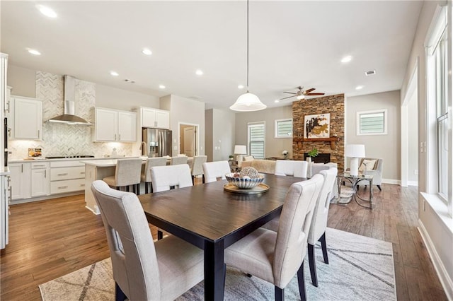 dining area featuring baseboards, light wood-type flooring, a stone fireplace, recessed lighting, and a ceiling fan