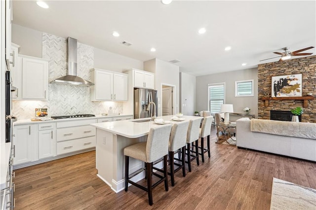 kitchen with a fireplace, stainless steel fridge, gas stovetop, wall chimney exhaust hood, and a sink